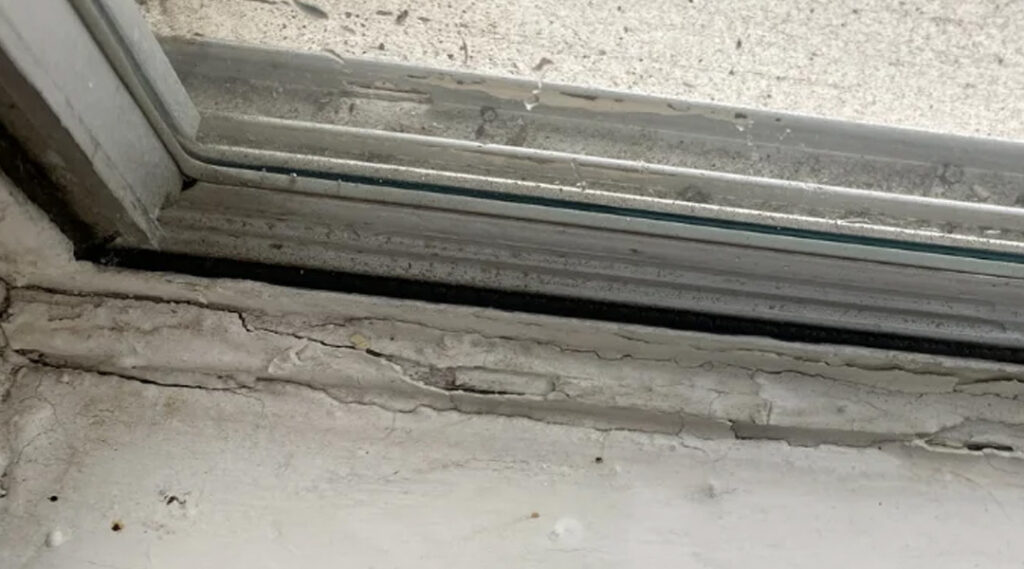 Old window frame with cracks and poor sealing causing energy loss in Perris CA home