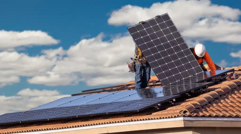 Solar installers placing panels on a tile roof under a sunny sky